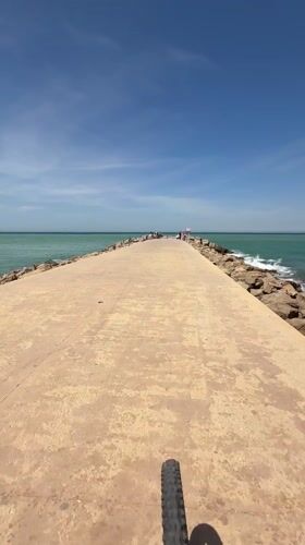 Cyclist rides concrete pier amid turquoise waters in Tangier