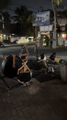 Street musicians set up a suspended gong on a Kuta sidewalk at night