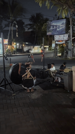 Street musicians set up a suspended gong on a Kuta sidewalk at night