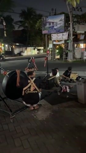 Street musicians set up a suspended gong on a Kuta sidewalk at night