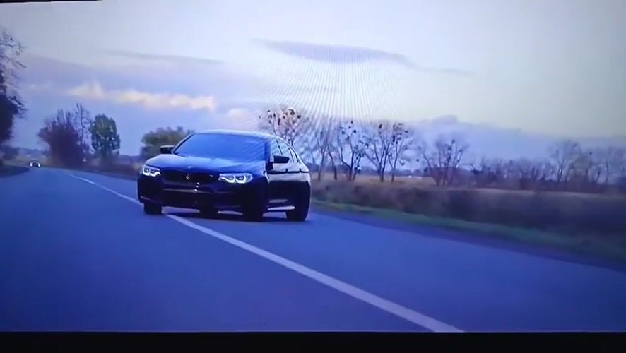 Black BMW travels rural road in Nizhnevartovsk under overcast skies
