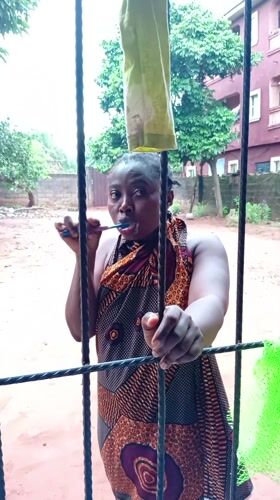 Woman brushes teeth behind fence in Nkpor, Nigeria