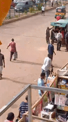 Busy open-air market street with vendors, vehicles, and foot traffic