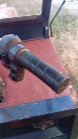 A close-up shot shows a handlebar on a three-wheeled vehicle. The handlebar is black and has various switches and a grip. The vehicle's interior, which is red and appears to be made of a worn material, is visible. The shot also captures a partial view of the vehicle's windshield and exterior, suggesting it is outdoors. The camera pans to the left and right, revealing more of the handlebar and the vehicle's interior.