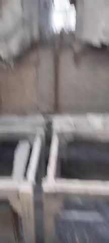 The video shows a panning shot of an abandoned industrial building. The interior is dilapidated with exposed beams and pipes. The exterior shows a long, decaying structure with a smokestack in the distance. The overall impression is one of decay and disuse.
