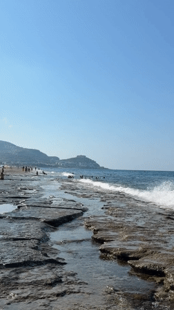 Rocky shoreline, breaking waves, and swimmers on a sunny day