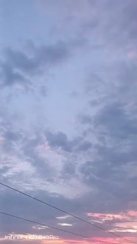 The video shows a sky filled with clouds, with the sky closer to the horizon showing pink hues from what appears to be either sunrise or sunset. There are overhead wires visible in the lower left corner of the frame. The clouds are mostly gray and white with some variations in density and texture. A treetop appears in the lower right corner towards the end of the video. The text "Infinix NOTE 40Pro" is seen in the bottom left corner of the screen.