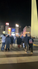 Pedestrians cross street toward lit obelisk in Buenos Aires