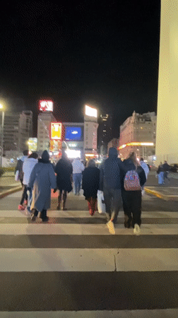 Pedestrians cross street toward lit obelisk in Buenos Aires