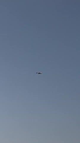 A video shows a clear sky with an airplane in the distance. The camera then pans to trees and a sunset.