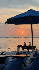 Horseback riders pass a beachside sunset setup in Indonesia