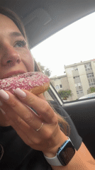 Woman enjoys pink sprinkled donut in car, Budva
