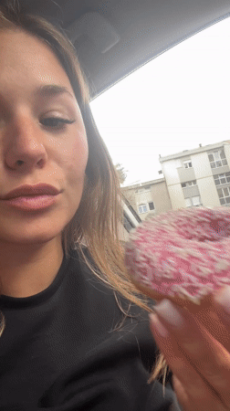 Woman enjoys pink sprinkled donut in car, Budva