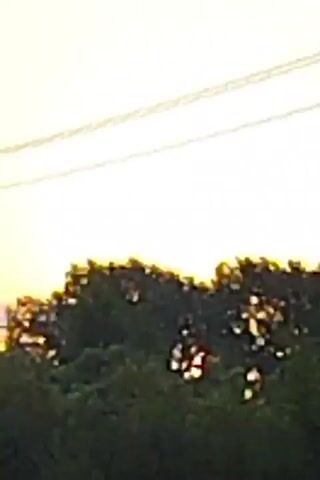 The video shows a sunset with clouds and trees. There are power lines in the sky and a telephone pole. The video is in landscape mode and the resolution is low.