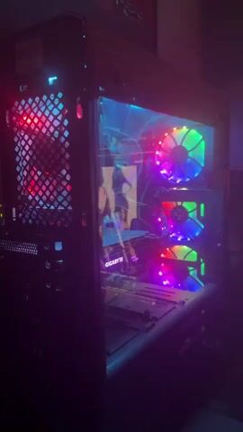 A computer tower with RGB lighting is shown from the side. The front of the tower has three fans that are lit up with various colors. The side panel of the tower is clear, allowing a view of the internal components, which are also illuminated with colored lights. The computer appears to be turned on.