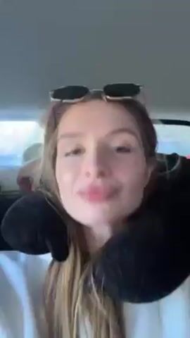 The video shows a woman wearing sunglasses and a neck pillow, likely sitting in a car. She looks directly at the camera and makes various facial expressions.  Music is playing in the background.