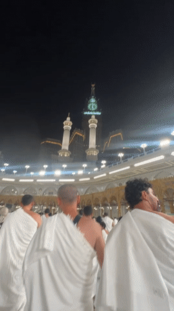 Pilgrims in ihram move through Mecca near the Kaaba at night