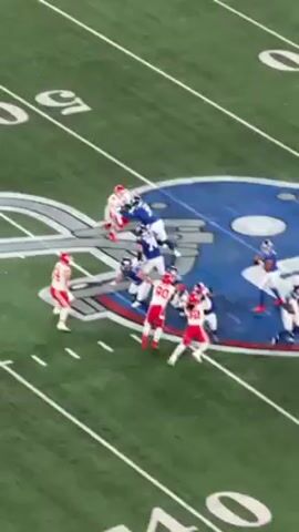 The video shows an American football game from an elevated perspective. The focus is on a field goal attempt by a team wearing red and white uniforms. The team in blue tries to block the kick. The kicker successfully kicks the ball through the uprights. The goal post and the field markings are visible. Spectators are partially visible in the bottom of the frame. The video appears to have been taken with a phone camera.