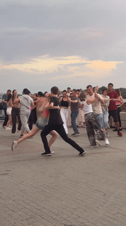 Outdoor social dancing on a waterfront plaza at sunset