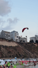 Red canopy paraglider soars over busy Netanya beach