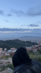 Person visits graffitied Barcelona overlook with white cross at dusk