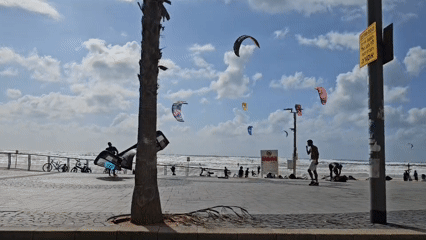 Busy beachside promenade with kitesurfers and cyclists captured
