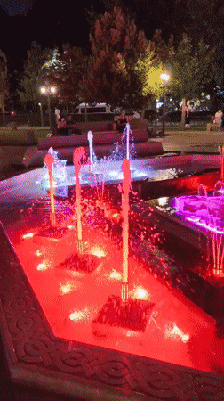 Lit-up fountain plaza at night with decorative lampposts
