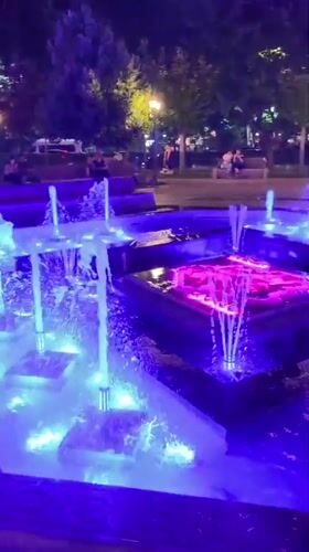 Lit-up fountain plaza at night with decorative lampposts