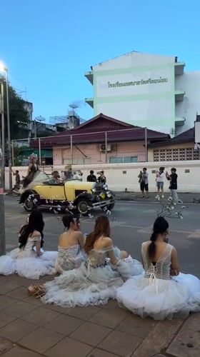 Women in formal gowns watch parade from Chiang Mai sidewalk