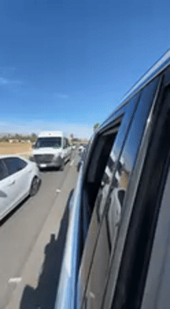 Woman in gold dress hangs from car in Indio traffic