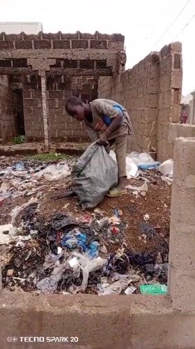 Youth collects trash among waste piles in Rigasa