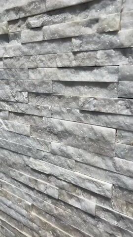 This is a close-up, still shot of a wall constructed from stacked stone tiles. The stones are predominantly white and gray, with visible veins and a rough, textured surface. The lighting creates subtle shadows that highlight the dimensionality of the stacked pattern. The perspective is slightly angled, showing the wall receding into the background. There are no people or any other objects visible in the frame.