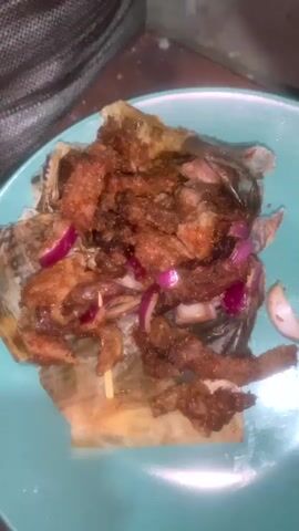 A plate with food, possibly meat and onions, sits on a turquoise plate. Next, a green soursop fruit is in an orange bowl. Finally, a bottle of red wine with a red cap is on a tray next to some brown food.