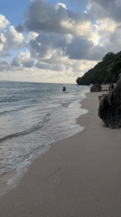 Beachgoers enjoy rocky outcrop amid cloudy Indonesian coastal scene