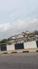 Motorcyclist travels road in Aso, Nigeria under overcast skies