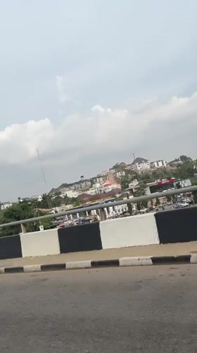 Motorcyclist travels road in Aso, Nigeria under overcast skies