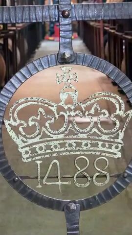 The video shows a gated entrance to a whiskey cellar. The metal gate is marked with a crown and the number 1488. The gate opens into a room lined with wooden barrels. A blue metal door is labeled "Tullibardine Distillery WH No. 4 Blackford." The room itself is a brick-lined cellar with rows of barrels. The lighting is dim and industrial. The ceiling is low and shows signs of moisture or mold. The video shows a wide shot of the barrel room.