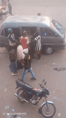Group gathers around gray van on littered pavement