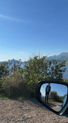 Vehicle mirror captures scenic Montenegro bay view with pedestrian