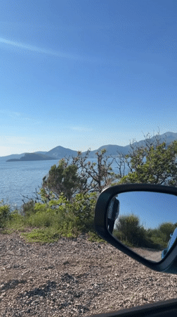 Vehicle mirror captures scenic Montenegro bay view with pedestrian