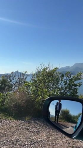 Vehicle mirror captures scenic Montenegro bay view with pedestrian