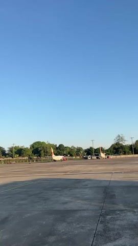 The video shows an airport tarmac on a clear, sunny day. Two airplanes are parked in the background. In the foreground, a white Lion Parcel ATR 72-500 aircraft is visible. People are boarding the plane, carrying bags and luggage. The camera pans to the tail of the plane, focusing on the red lion logo. The tail number PK-WFK is visible on the plane's body.