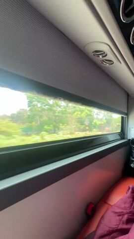 The video shows the interior of a vehicle, likely a bus or a private transport. Initially, the view is through a window showing trees and passing scenery. A hand reaches up and pulls down a gray window shade, completely blocking the outside view. The camera then pans upwards in the darkness, revealing the ceiling and a small screen displaying icons. The screen is the main source of light in the otherwise dark interior.