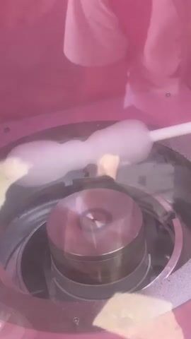 Inside a pink cotton candy machine, a hand holds a plastic cup to catch the cotton candy as it is spun.