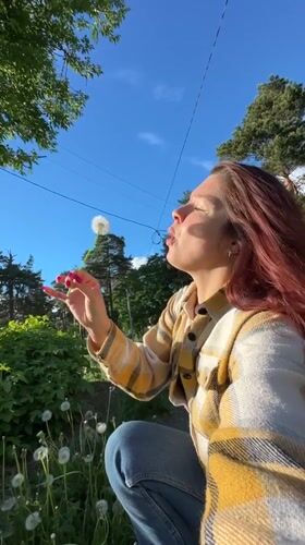 Woman blows dandelions in Vladimir field amid spring afternoon
