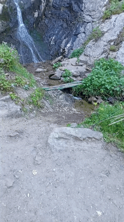 Small waterfall flows down vegetated cliff in Ustina, Bulgaria