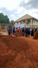Funeral gathering observed outside building with burial evidence