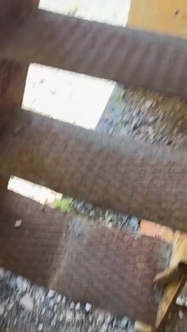 The video shows an interior view of a dilapidated, multi-story structure. The perspective is from a lower level looking upwards through rusted metal staircases. The walls appear to be concrete or stucco, some with exposed brickwork. There are openings and holes in the ceiling, suggesting structural decay. The overall impression is one of abandonment and disrepair. The lighting suggests it is daytime, with natural light entering through the openings. No people or animals are visible.