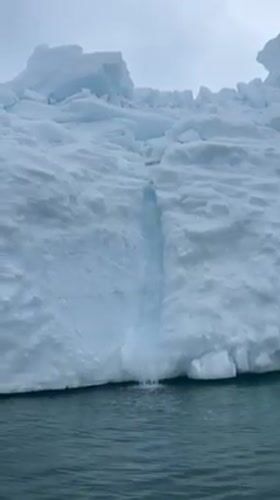 Antarctic iceberg captured with waterfall cascading into ocean waters