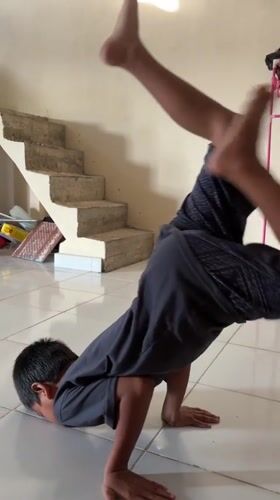 Boy practices breakdancing moves indoors while cat watches